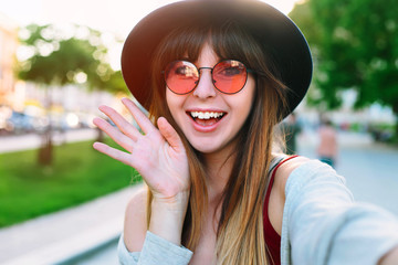 Wall Mural - Young smiling teen happy woman making selfie on the street Smiling girl talking on video chat mobile phone app or taking selfie photo for social media. Carefree and happy, sunny spring mood. 