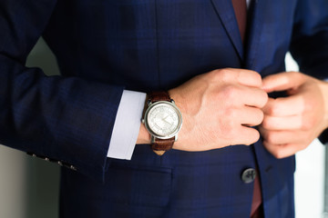 Closeup fashion image of luxury watch on wrist of man.body detail of a business man.Man's hand in  pocket closeup at white background.Man wearing blue jacket and white shirt and tie.