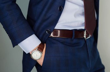 Wall Mural - Closeup fashion image of luxury watch on wrist of man.body detail of a business man.Man's hand in blue pants pocket closeup at white background.Man wearing blue jacket and white shirt.Not isolated