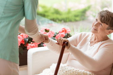 Wall Mural - Doctor helping an elderly woman with Parkinson's disease get up from a sofa in a rehabilitation facility