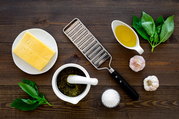 Ingredients for pesto sauce. Cheese, garlic, green basil, olive oil, salt near grater and mortar on dark wooden background top view