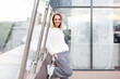 © Rithor - Portrait of cheerful charming young stylish independent woman standing on the top floor of a modern business center on an outdoor terrace. Businees people concept, city life, trendy person, youth