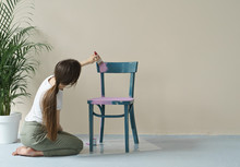 Young Woman Painting Chair In Pink At Home