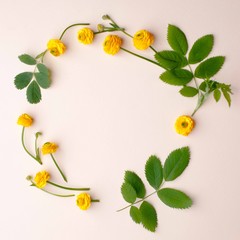 Flowers composition. Wreath made of various yellow flowers and green leaves and branches on pastel yellow background. Flat lay, top view, copy space, square