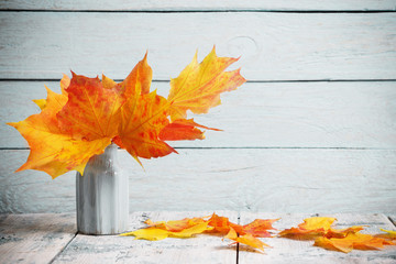 autumn yellow leaves in vase on old wooden background