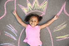 Little African-American Child Lying Near Chalk Drawing Of Wings And Crown On Asphalt, Top View