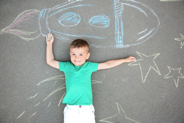 Poster - Little child lying near chalk drawing of rocket on asphalt, top view