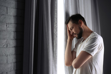 Lonely depressed man near window at home