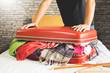 man trying to fit all clothing to packing his red suitcase before vacation.