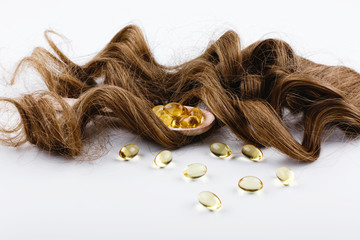 Oil capsule for hair with vitamin E lie on wooden spoon on brown hair curls