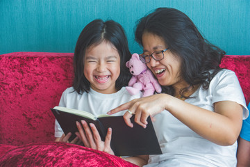 young mother and little daughter girl reading a book on sofa at home