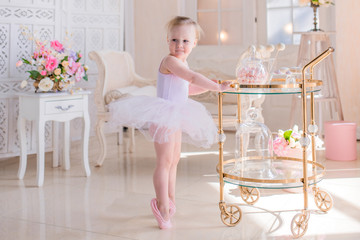 charming little girl dressed like a ballerina poses in a bright room with shiny lamps