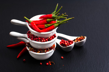 Wall Mural - Red color Exotic spices concept  red chilies, pink peppercorn and mix of ground chili pepper on balck slate stone with copy space