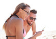 © ASDF - Smiling couple browsing their photos on the beach
