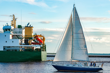 Canvas Print - Blue sailboat against cargo ship