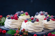 Homemade meringue basis for cake Pavlova with fresh blueberries and BlackBerry and powdered sugar on black concrete texture background. Copy space