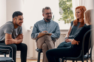 Smiling spanish man talking with friends during meeting for teenagers with therapist