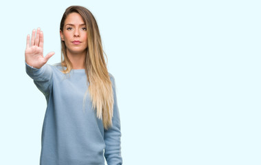 Wall Mural - Beautiful young woman wearing sweater and jeans with open hand doing stop sign with serious and confident expression, defense gesture