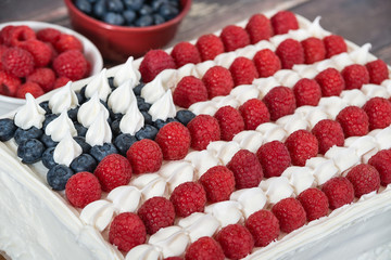 Patriotic, red white and blue, American flag cake. Fresh blueberries and raspberries in the background. Concept for Fourth of July celebration.