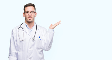 Sticker - Handsome young doctor man smiling cheerful presenting and pointing with palm of hand looking at the camera.