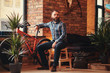 © Fxquadro - Handsome bearded hipster male in a blue fleece shirt and jeans sitting on a wooden stool at a studio with a loft interior.