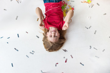 Happy little girl lays on the floor in confetti and metaphane