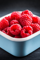 Wall Mural - Raspberries fresh arrangement in blue ceramic jar on black table close up in studio