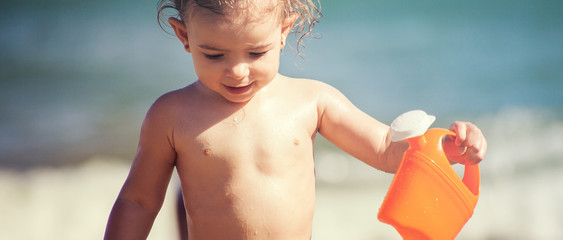 Cute little girl holding toy watering can on the beach, letterbox