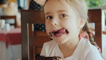 A Cool Little Girl Is Eating A Sweet Bun, Her Face Is Smeared With Chocolate