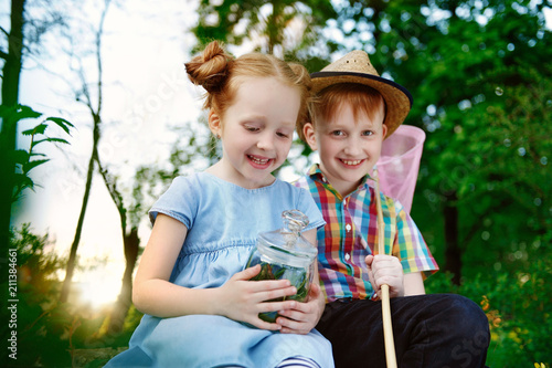 Two Red Haired Kids Catching Insects In A Forest With A Jar And