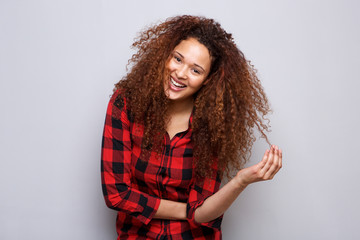 Wall Mural - cheerful young woman smiling against gray background with hand in curly hair