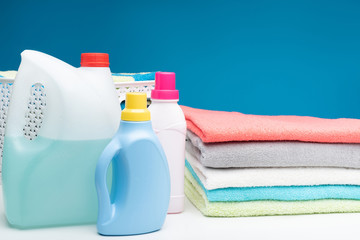 Close up of white table with bottles of fabric liquids. Fluffy colorful textile with plastic basket full of cotton linens is aside