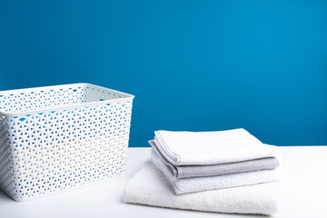 Close up of half empty basket for dirty clothes lying on white board. Heap of light terry towels is nearby