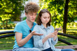 © byswat - Young couple of students. A guy with a girl summer park in nature. They sit on a bench in city. In hands holds a smartphone. Emotions of surprise . The concept frustration is frustration from result.
