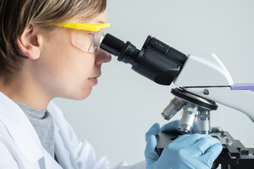 Wall Mural - young female scientist looking through a microscope in the laboratory.