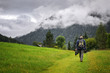 Cloudy summer landscape in Austria, a man hiking through a meadow covered with a little yellow flowers, mountains with pine forest, rainy clouds