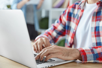 Wall Mural - Man`s hands keyboard on laptop computer sits at spacious office. Unrecognizable man freelancer uses modern electronic device for distant work, reads information from web page, uses internet.