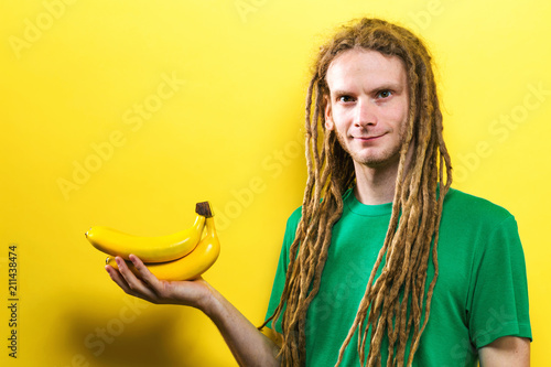 Fotografie, Obraz Happy young man holding bananas on a yellow background