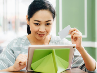 Happy woman is using a white mockup credit card for online shopping on tablet.