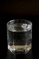 Glass with clear water on a black background. Vertical photo