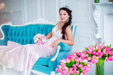 lovely bride in pink dress and with diadem, lies on couch, in white room with fireplace