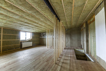 Construction and renovation of big light spacious empty room with oak floor, walls and ceiling insulated with rock wool, heating radiators under low attic windows and wooden frame for future walls.