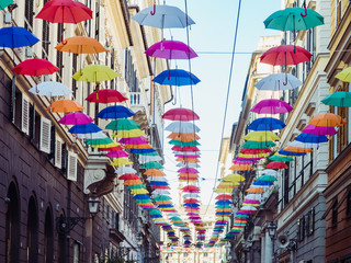 Multicolored, bright umbrellas hanging between houses on the beautiful, narrow streets of the magnificent city of Genoa against the blue sky, on a sunny, summer day. Concept of travel and recreation