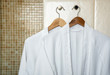 Two white rag bathrobes towels on wooden hangers in the interior of a stylish bathroom. Relax in the hotel for two.