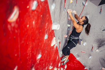 Wall Mural - Young unrecognizable woman in black sportswear doing professional bouldering on grey and red rockat climbing gym indoors