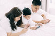 © ic36006 - Asian boy playing smartphone with young parents lying in bed.Happy famility