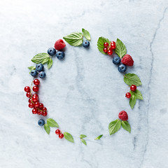 Wall Mural - An Arrangement of fresh raspberries, blueberries, red currant and mint leaves on gray marble background. Flat lay. 