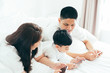 © ic36006 - Asian boy playing smartphone with young parents lying in bed.Happy famility