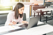 © Andrei - Focused young woman working in office, sitting at desk, using laptop, holding the phone
