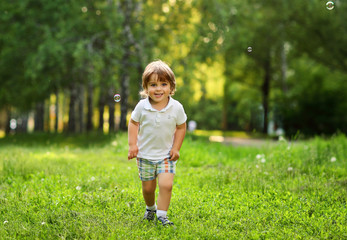 A 2 year old boy plays outside in the summer for soap bubbles.